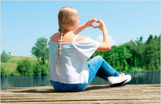 Mädchen sizt im Wald an einem Steg mit ihrem coocazoo Schulrucksack und zeigt mit ihren Händen ein Herz in die Luft