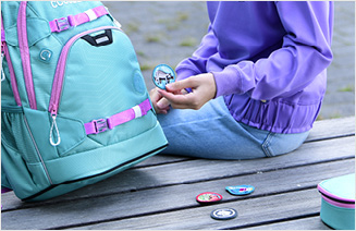 Kind individualisiert seinen Schulrucksack mit vielen bunten Schnallen, Zippern und Klett-Patches